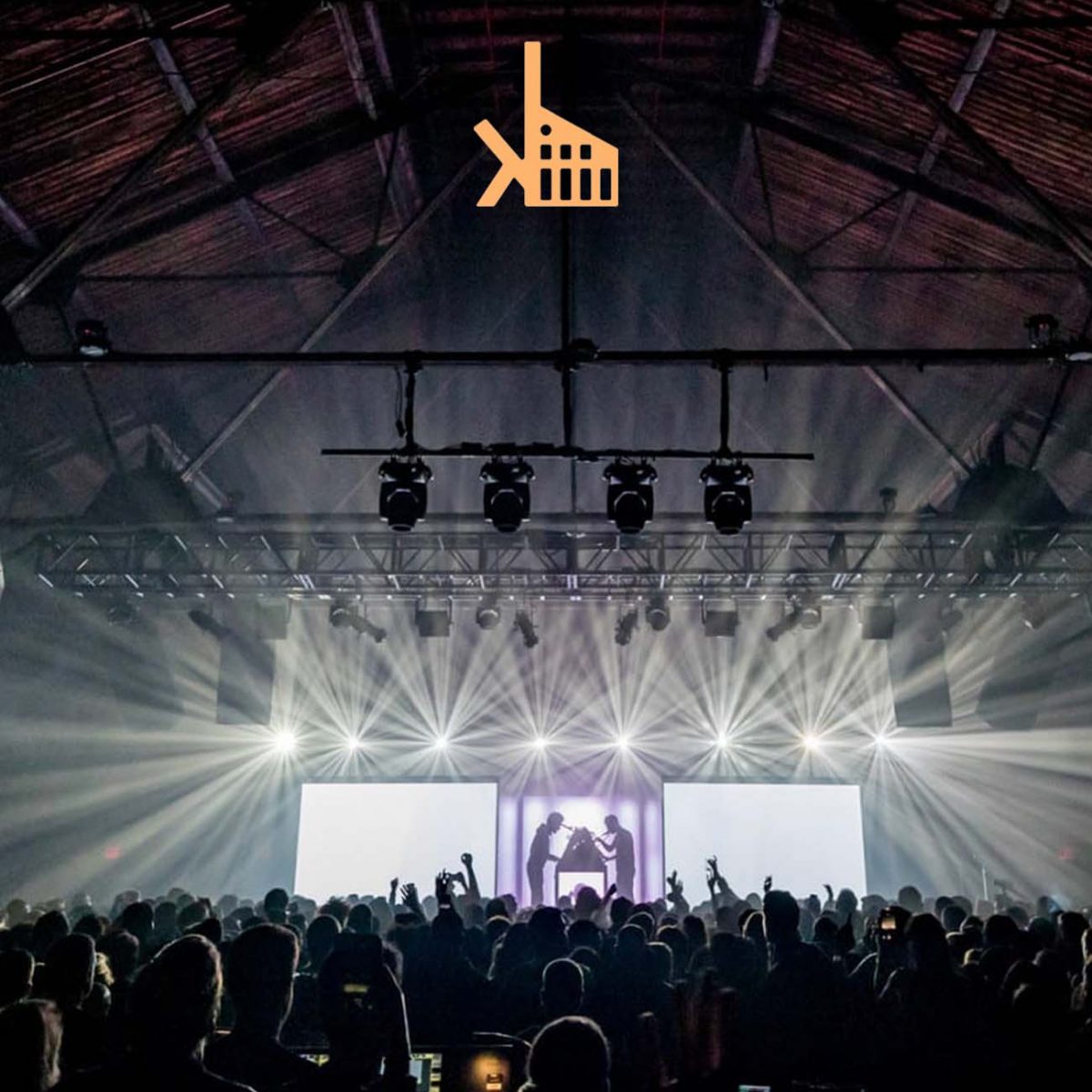 Music venue with thousands of fans in front of backlight stage with two performers. Yellow Knockdown Logo top center.